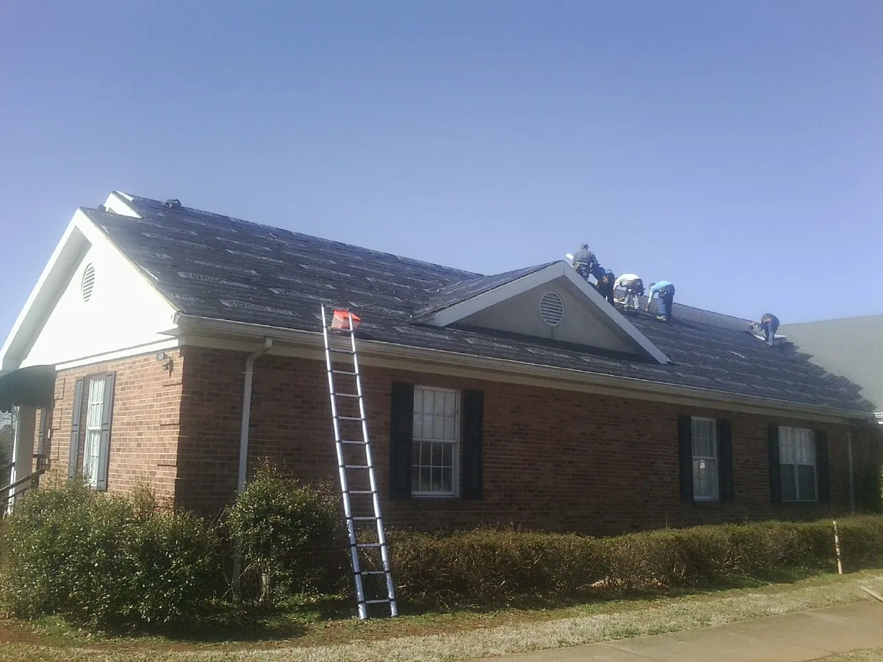Crew tearing shingles off a brick ranch roof with a ladder set — Emergency Roof Repair work by our crew in California
